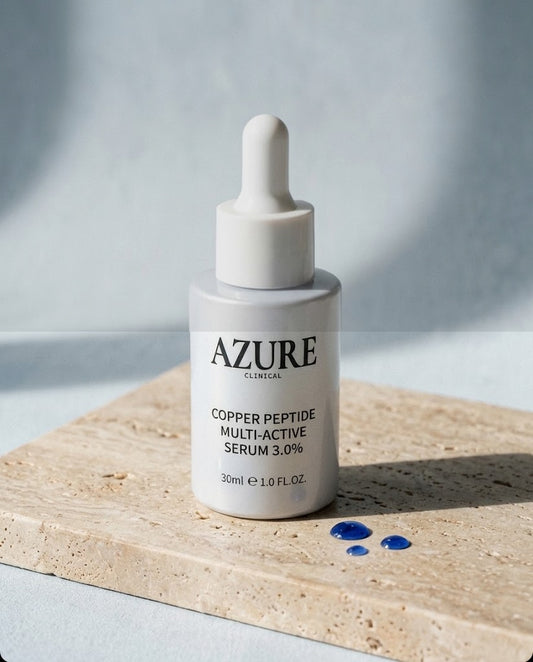 Azure Clinical Copper Peptide Multi-Active Serum 3.0% dropper bottle on travertine stone with cobalt-blue serum drops